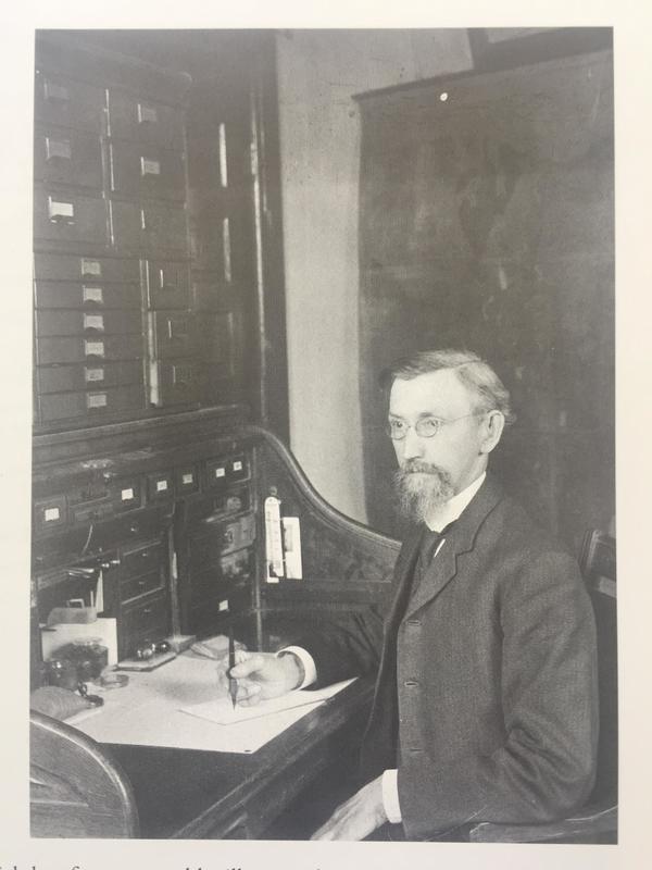 Charles E. Thorne sitting at a desk, signing a piece of paper. 