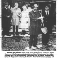 People gathered around a man wearing a hard hat and holding a shovel. 