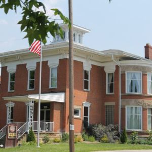 A side view of a large,  two-story brick house with a tower and a large front porch which is the elk lodge