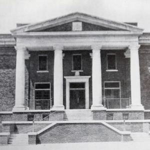 Front view of a large hall with four white pillars and a high roof. 