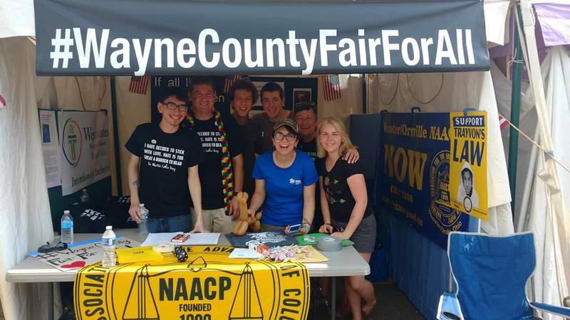 Seven people pose together in a booth under a banner that says "#Wayne County Fair For All" 