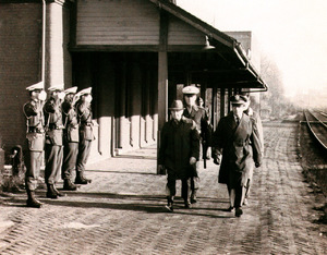 Soldiers salute as a group of men walks by them at the train station. 