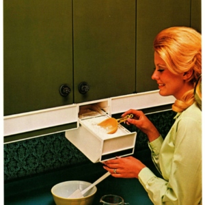 A woman scoops flour out of a drawer on her kitchen cupboard. 