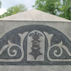 A symbol of an eagle standing on two rivals, a flag, and a large star engraved on a headstone 