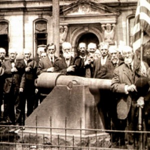 A large crowd gathers around a canon and an American flag in front of the courthouse