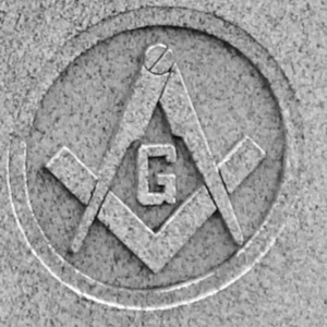 A stone engraving of the masonic symbol, which is a compass pointing downward and a 90 degree angle ruler pointing upward with a "G" in the middle 