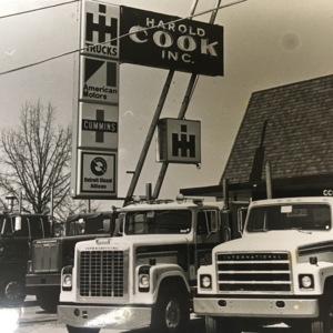 A view of a building with a sign in front of it that says "Harold Cook Inc." and 18-wheeler trucks parked in front of it. 