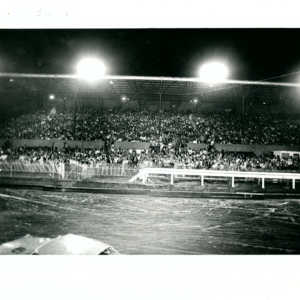 Hundreds of people sitting in the stands watching the car race track. 