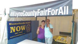 Two women pose in a booth underneath a banner that says "#Wayne County Fair For All"