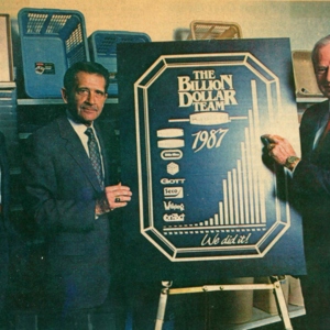 Two men stand next to a sign that says "The Billion Dollar Team 1987" 