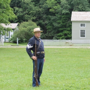 Civil War reenactor stands at attention, holding a rifle and wearing a military uniform. 