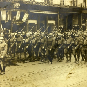 Soldiers in uniform and carrying guns marching down the street. 